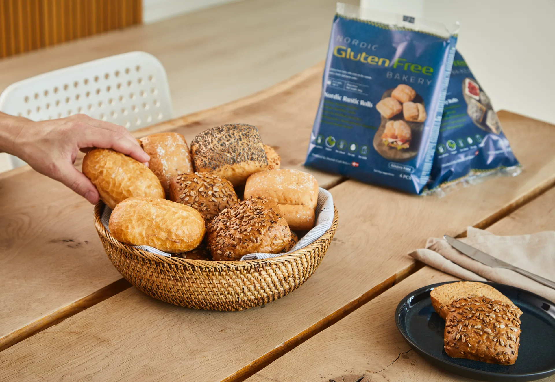 Assorted Gluten Free Nordic rustic rolls in a basket next to Nordic Gluten Free Bakery retail packaging